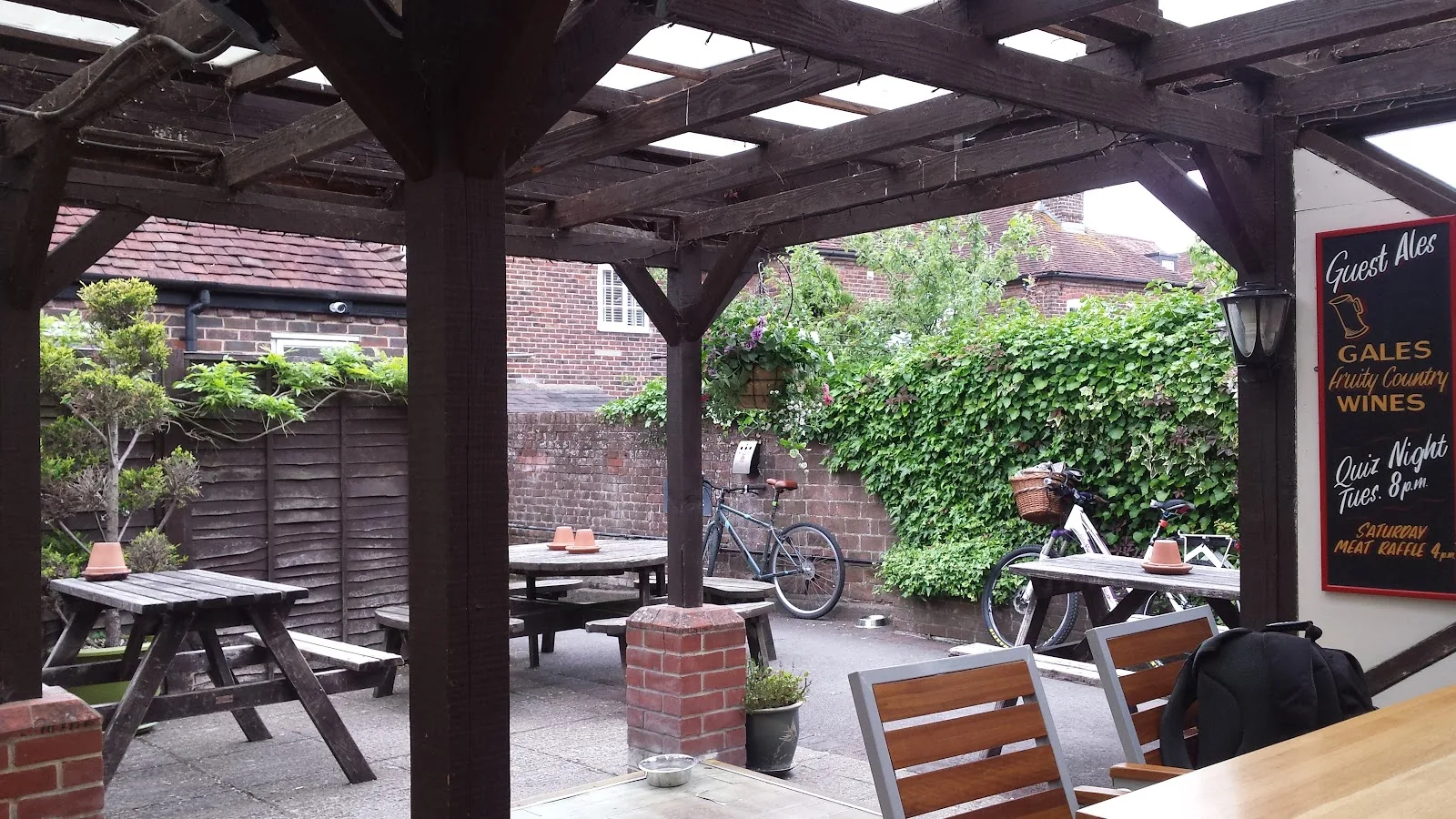 The covered garden at The Robin Hood with picnic tables under a timber pergola and a chalkboard listing guest ales and events